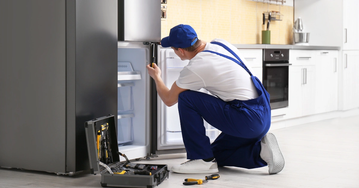 Appliance repair technician in uniform using a screwdriver to fix refrigerator door hinges.