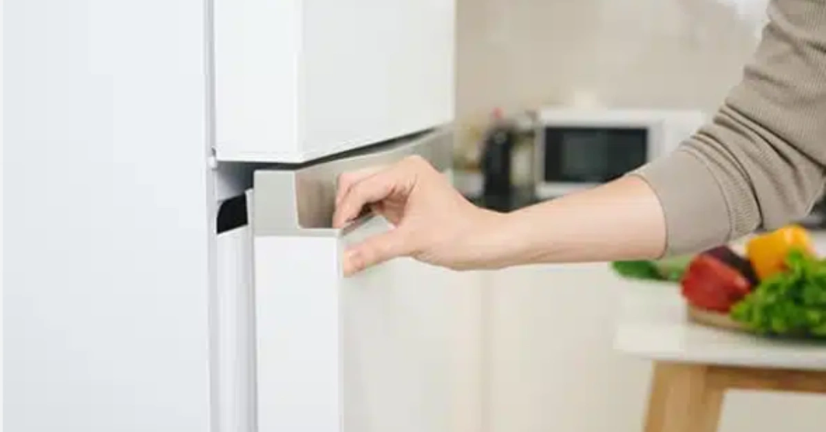 A close-up of a person's hand trying to close a white refrigerator door not sealing correctly.